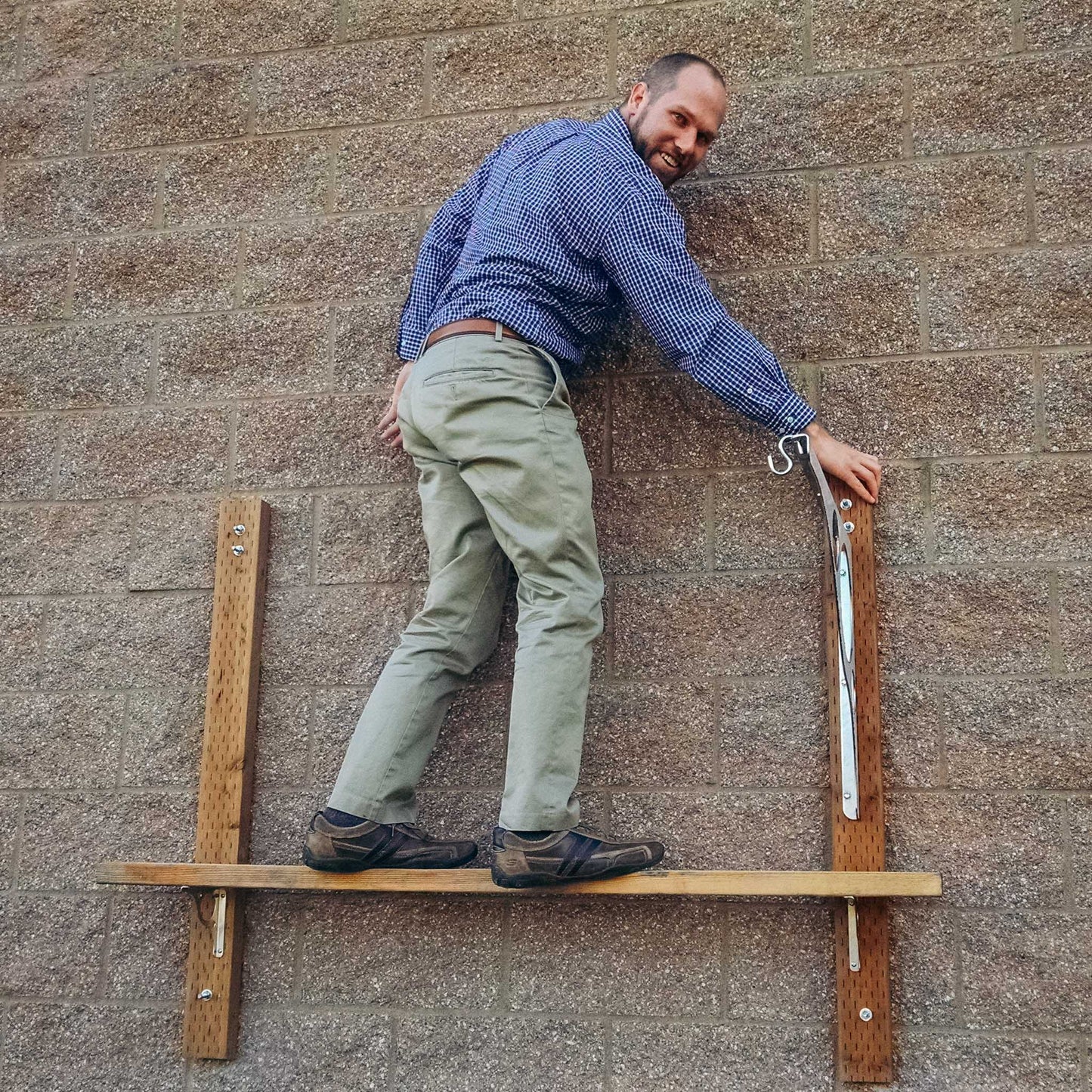 Cascade Manufacturing's Apex stainless steel shelf brackets attached to concrete brick wall with a man standing on them to demonstrate how strong our brackets are when properly installed into studs. Don't do this.